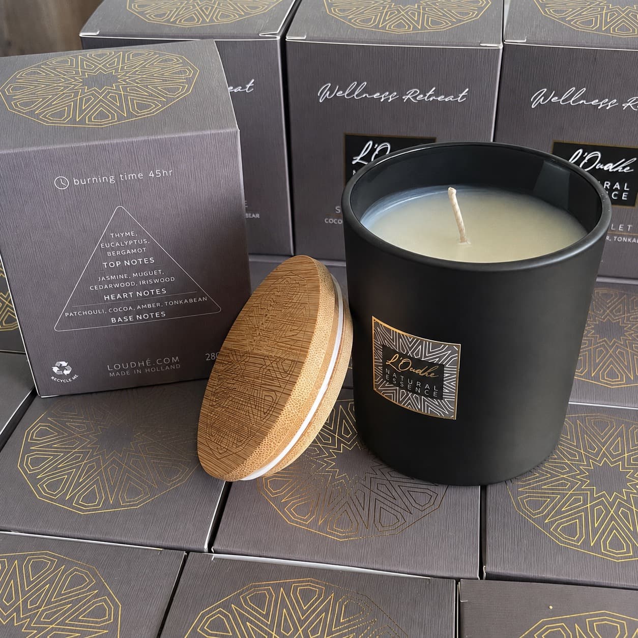 Wellness Retreat open with its lid leaning against the jar, set on a field of boxes printed with the gold zellige medallion, the scent pyramid visible.